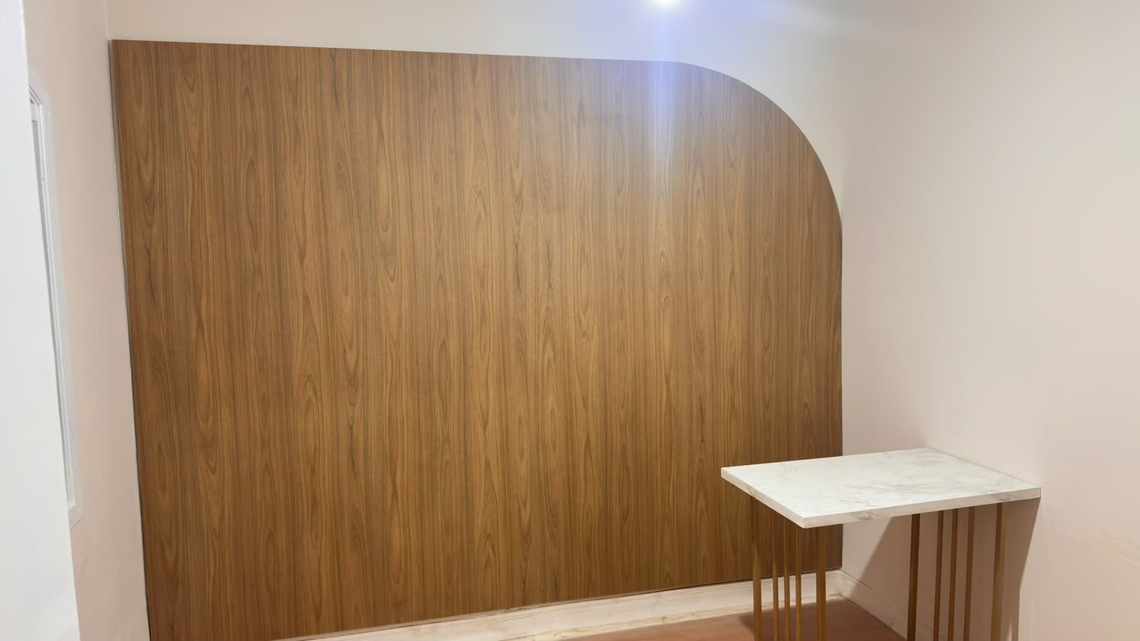 Painel de parede em amadeirado com mesa de tampo marmorizado e pés dourados